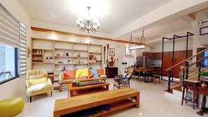 A spacious living room with a sofa, coffee table, and a wooden bench. There is a dining area with a table and chairs, and a staircase with a railing. - Professor's House 2198 (Ji'an)