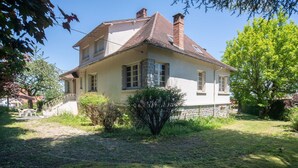 A two-story house with a stone foundation, a tiled roof, and a small front yard with a bush and a pathway leading to the entrance. - Quaint Holiday Home with Garden (Payzac)