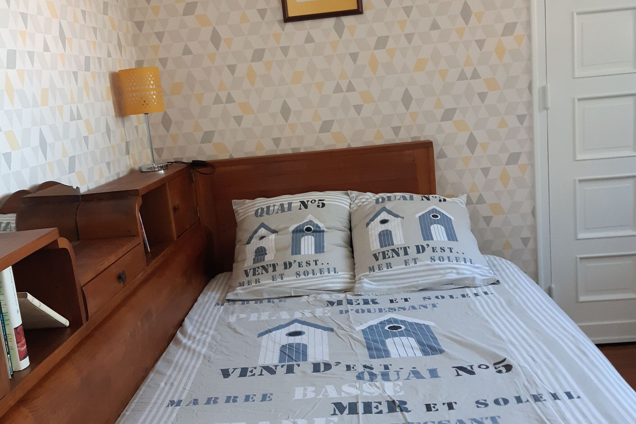 Ein Schlafzimmer mit einem hölzernen Bett, dekorativer Tapete, einer Nachttischlampe und einem Nachttisch mit Büchern.
