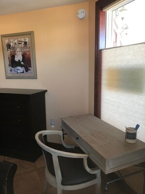 Ein Zimmer mit einem Holztisch, einem weißen Stuhl, einem schwarzen Schrank und einem gerahmten Bild an der Wand.