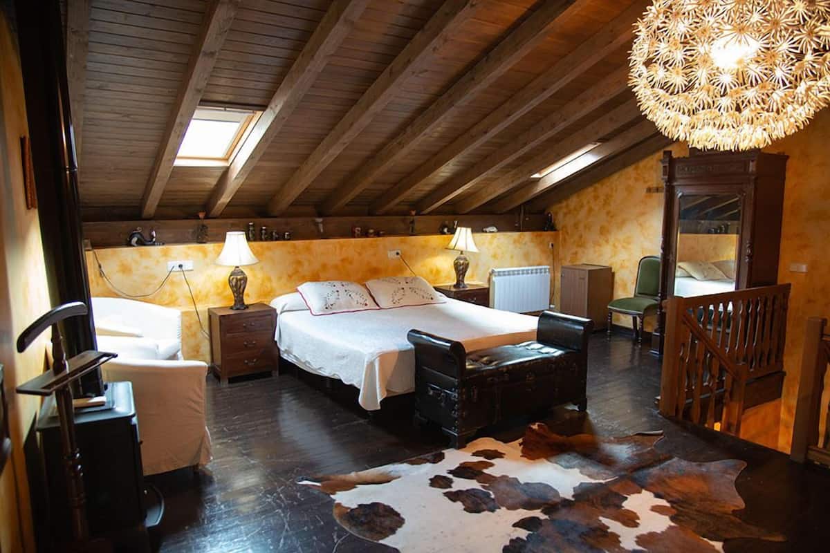 Un dormitorio acogedor con una cama grande, dos mesitas de noche con lámparas, un aparador de madera, un espejo y una alfombra de cuero de vaca.