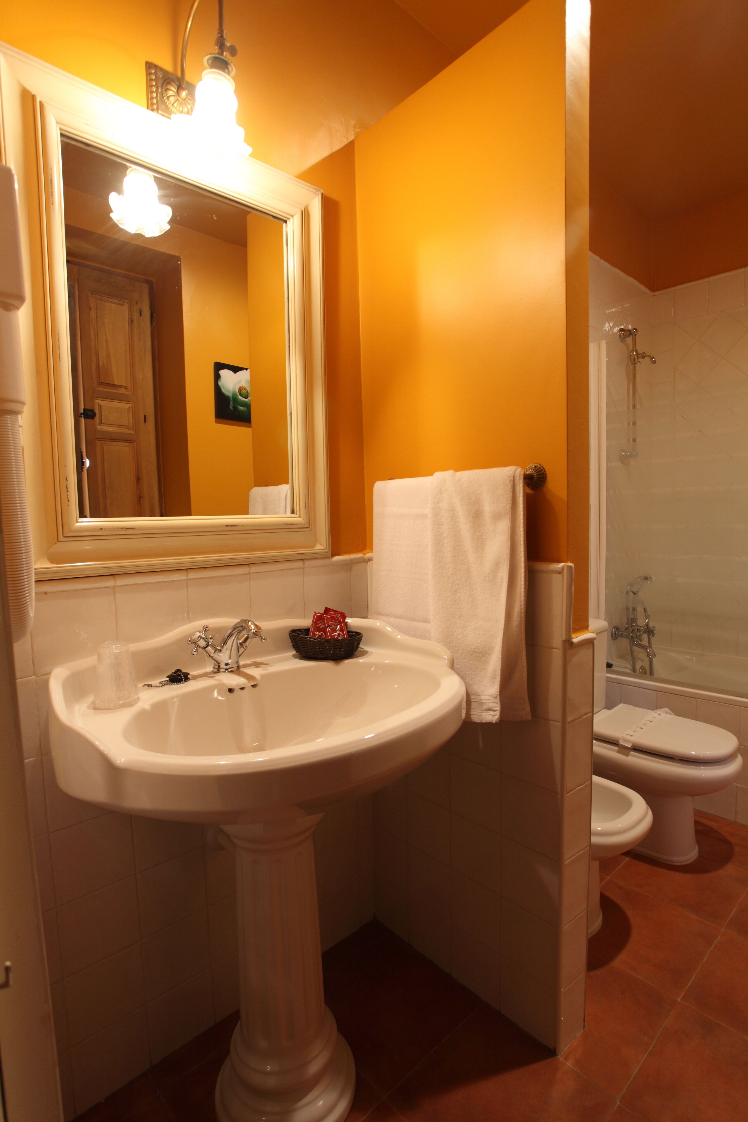 A bathroom with a pedestal sink, a mirror, a towel rack, a toilet, and a shower.