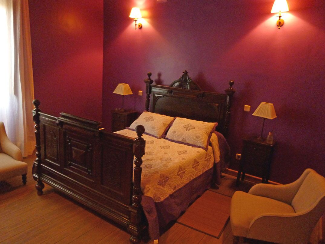 A bedroom with a four-poster bed, two bedside tables, a chair, and a lamp on each side of the bed.