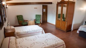 A room with two beds, a wooden wardrobe, and two green armchairs.