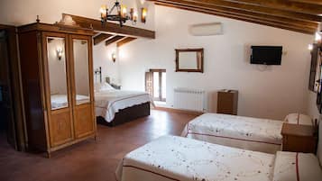 A bedroom with two beds, a wooden wardrobe, a mirror, a television, and a chandelier.