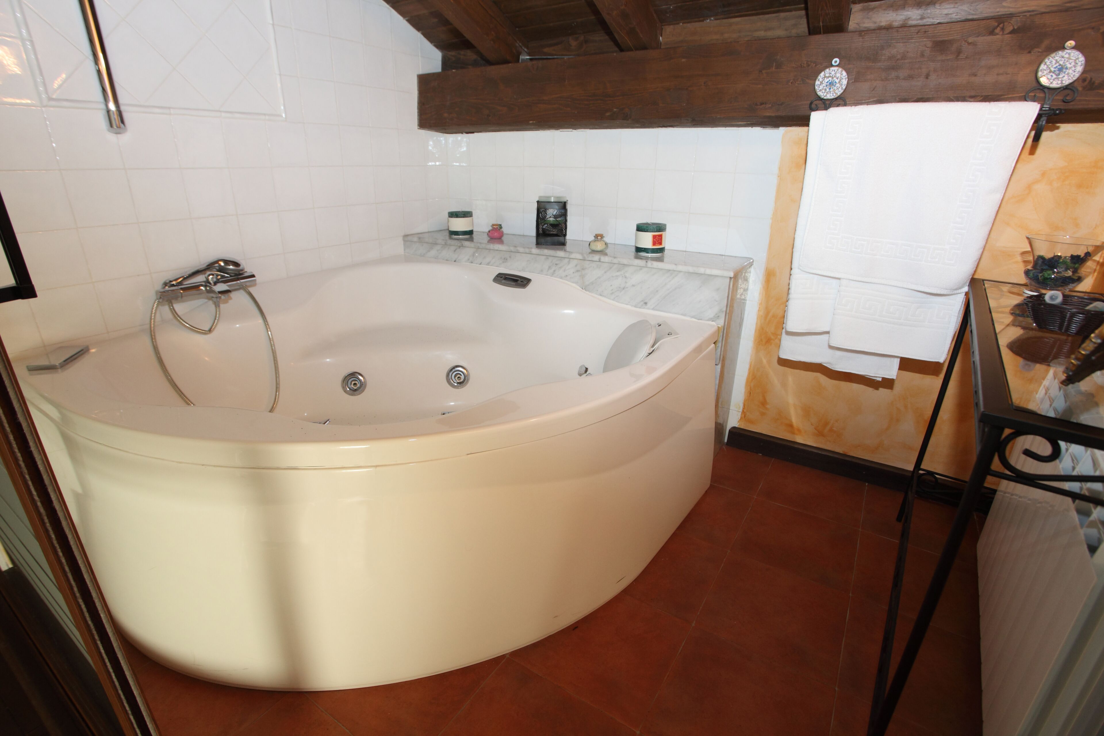 Een groot, vrijstaand bad in een badkamer met betegelde muren, een houten plafond en een betegelde vloer.