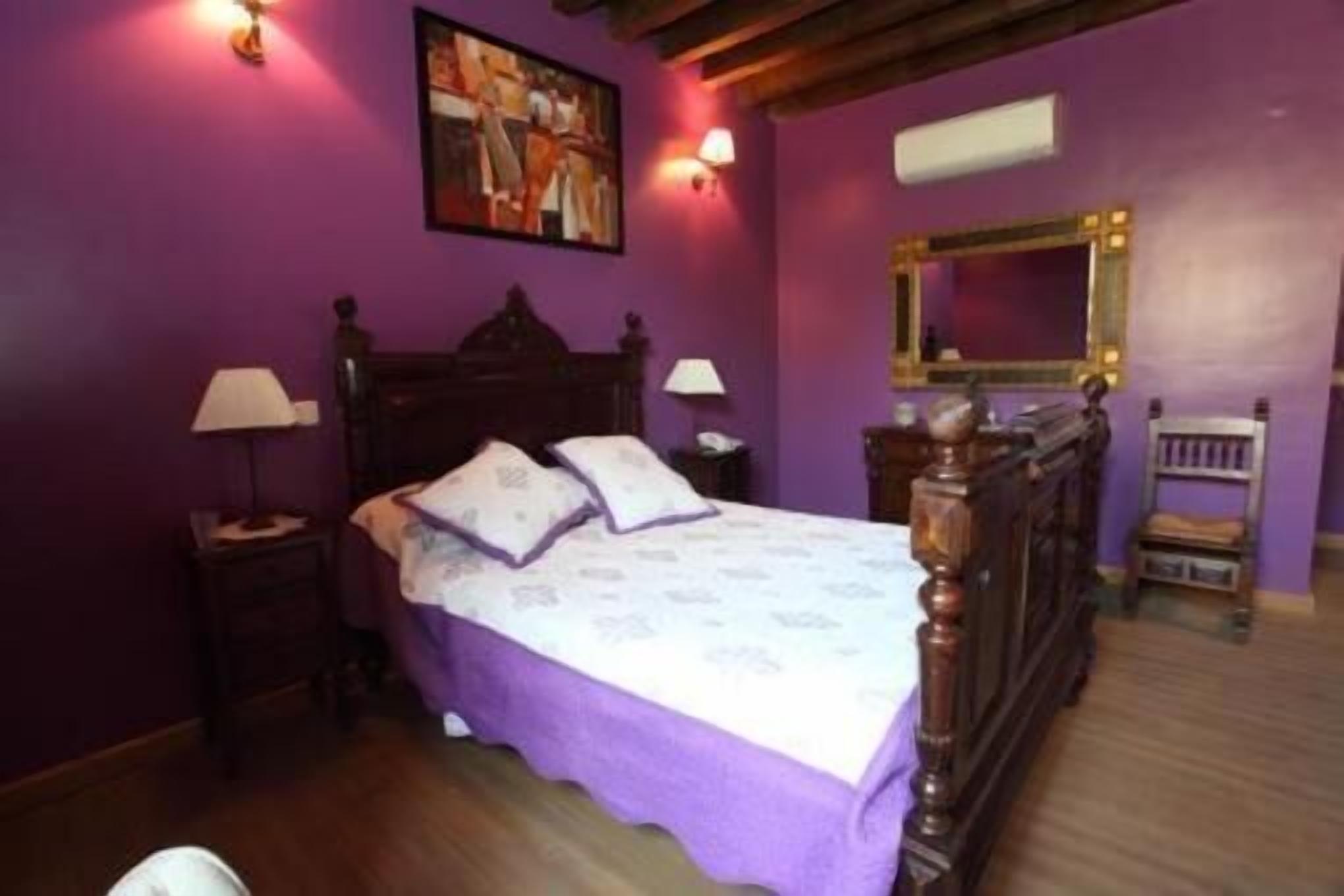 Un dormitorio con una cama de madera, paredes moradas y un cuadro sobre la cama.