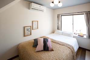 Um quarto com cama, ar condicionado, janela com cortinas e duas quadros na parede.