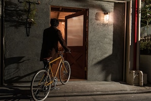 Uma pessoa se aproximando de um edifício com porta de madeira e uma placa com a inscrição 'BIKE TO BED'.