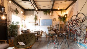A cozy, well-lit room with a large window, a green chair, a dining table, and several bicycles.