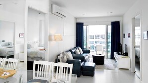 A modern hotel room with a dining area, a living room with a sofa and a TV, and a balcony with a view of the city. - SEACRAZE D709 - 2 Bedroom - Near Beach (Hua Hin)