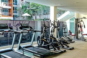 Una palestra con diverse macchine per esercizi, tra cui tapis roulant e cyclette, e vista su un edificio e del verde circostante.