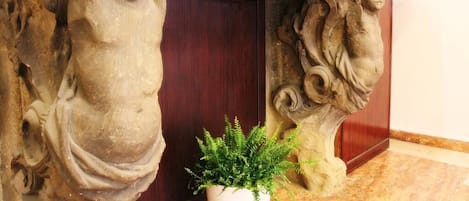 Escultura em pedra de um anjo com uma samambaia em vaso ao lado.
