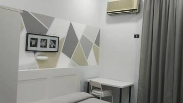 A hotel room with a bed, a small desk, an air conditioning unit, and a wall-mounted picture frame.
