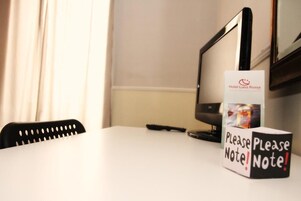 Una camera d'albergo con una scrivania, un monitor del computer e un cartello con su scritto 'Hotel Luna Rossa' e 'Attenzione'.