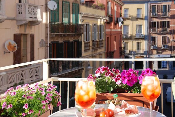 Un balcon avec une table dressée pour deux personnes, agrémenté d’un verre de vin rouge et d’une assiette de nourriture.