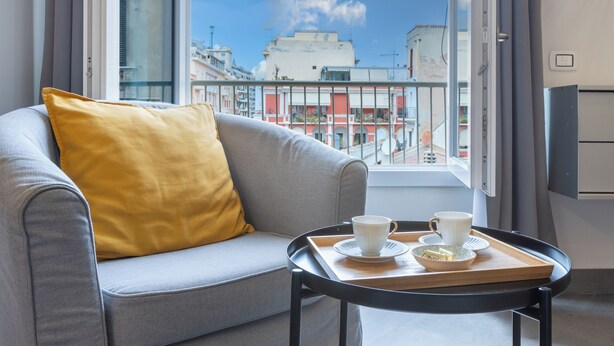 A modern hotel room with a grey sofa, a yellow pillow, and a tray with two cups and a bowl. - Centro Storico via Sassari Accommodation (Cagliari)