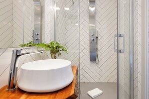 Une salle de bain moderne avec un lavabo blanc, un plan de toilette en bois et une cabine de douche en verre.