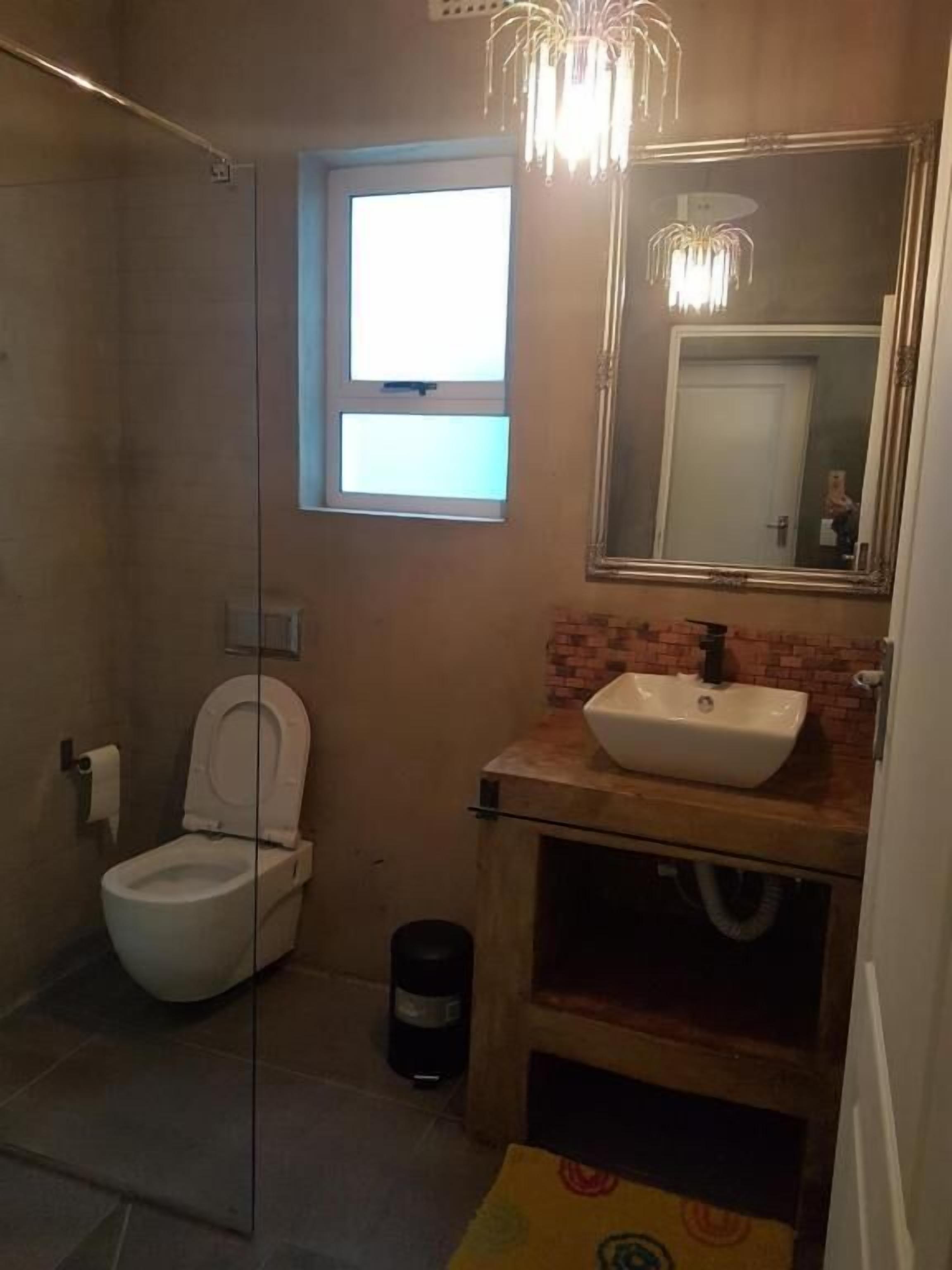 A bathroom with a toilet, a sink, a mirror, and a window.