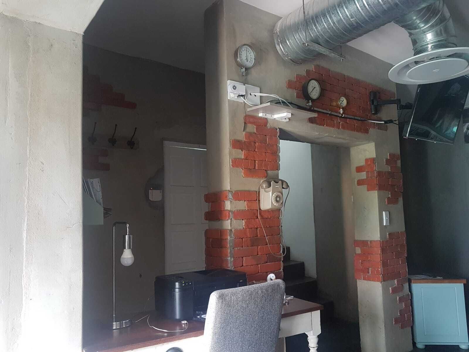 A room with a brick wall, a desk with a printer, a chair, and a radiator.