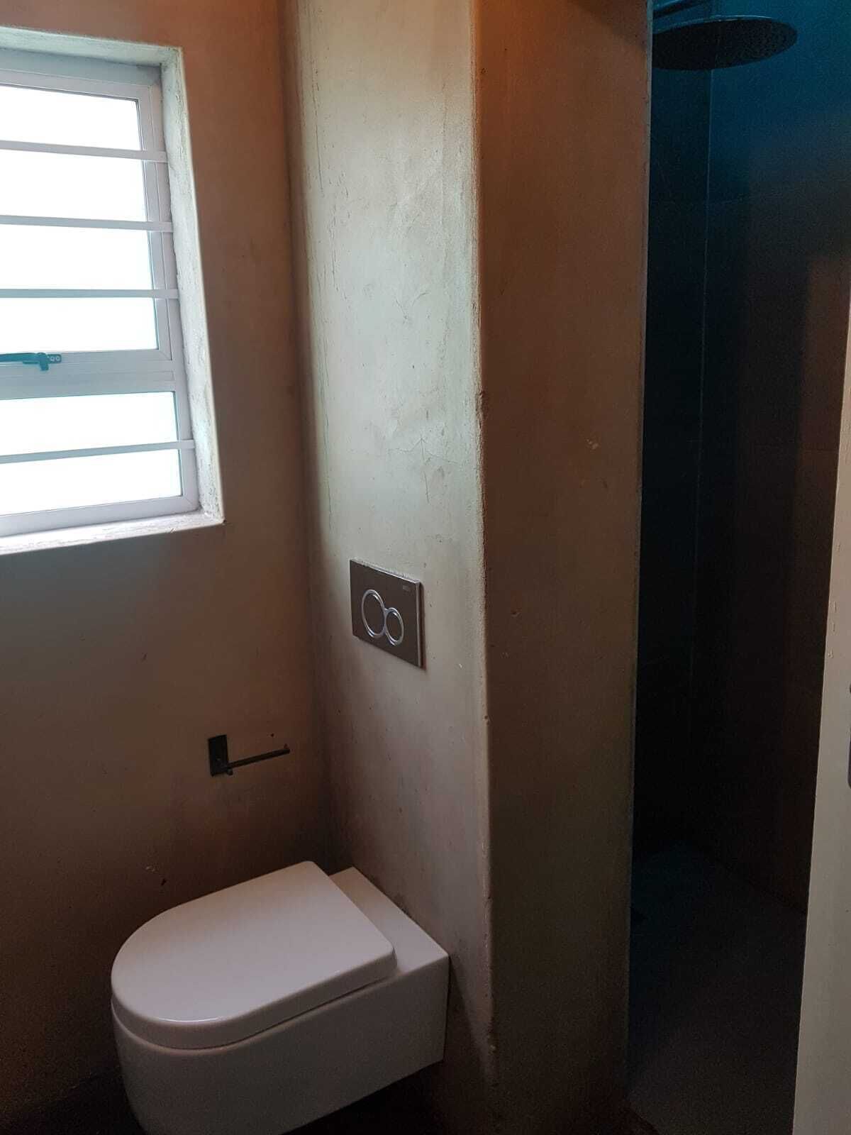 A small bathroom with a toilet, a window, and a shower area.