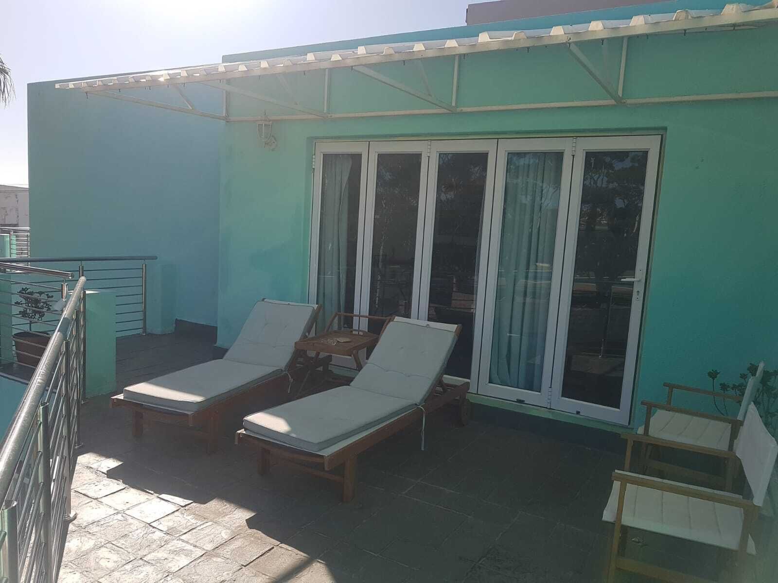 A balcony with two sun loungers and a small table, a sliding glass door, and a metal railing.
