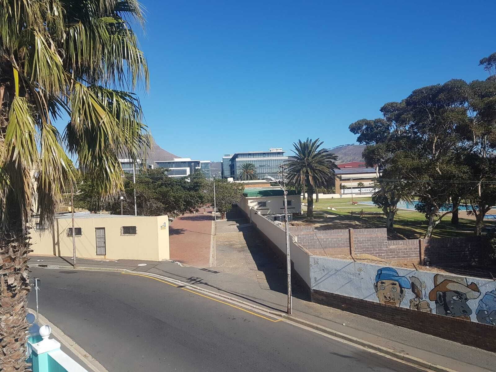 A road with a mural on the wall, palm trees, and buildings in the background.