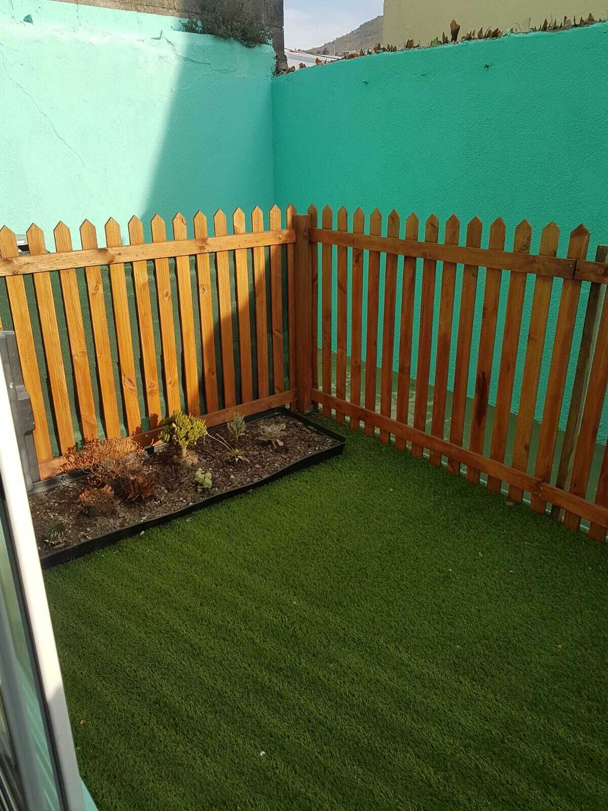 A small enclosed garden area with artificial grass and a wooden picket fence.