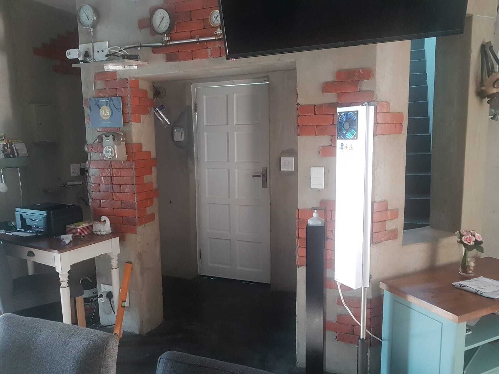 Una habitación con pared de ladrillo, una puerta blanca, un escritorio con impresora y una pequeña mesa con un jarrón de flores.