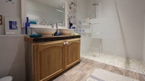 Un baño moderno con tocador de madera, un espejo grande, lavamanos y zona de ducha.