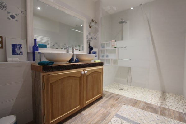 A modern bathroom with a wooden vanity, a large mirror, a sink, and a shower area. - Les Ateliers d'Art (Roanne)