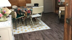 Un área de comedor con una mesa dispuesta para cuatro personas, rodeada de sillas de mimbre, un tapete estampado y un mueble de madera.