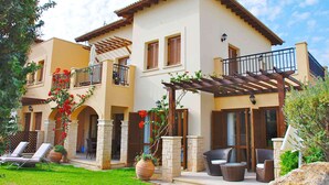 Una casa de dos pisos con un patio, mobiliario exterior y una pérgola.