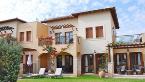 Una casa de dos pisos con balcón, un patio con muebles de exterior y un jardín.