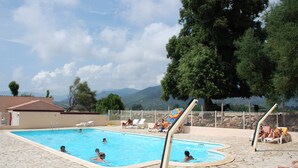 A swimming pool with people swimming and sunbathing, surrounded by stone tiles and a fenced area with lounge chairs. - Camping U Sommalu (Casaglione)