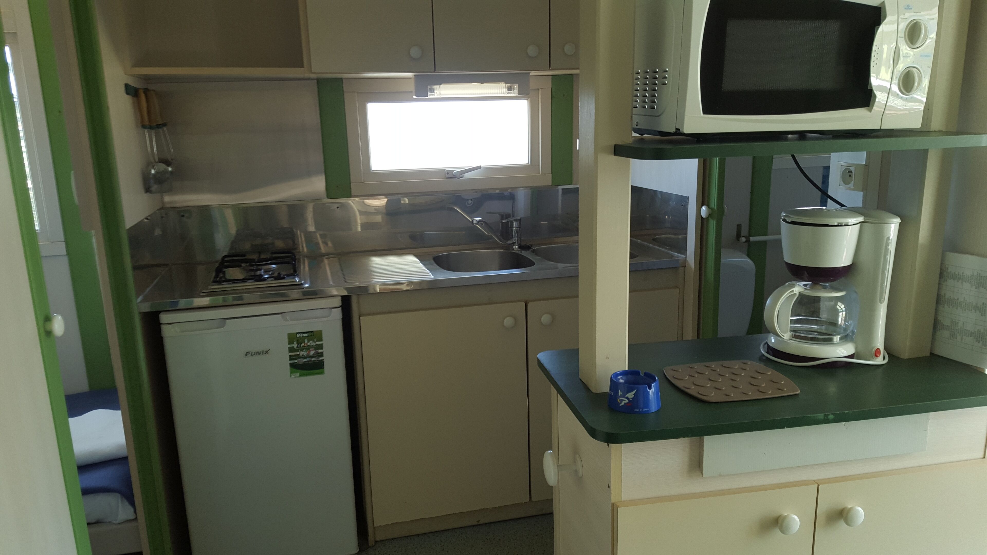 Una kitchenette compacta con estufa a gas, lavamanos, microondas y cafetera.