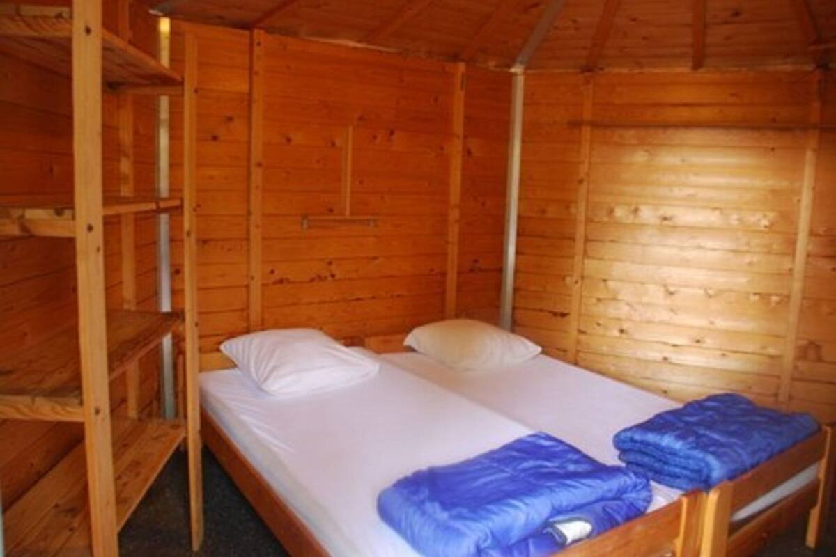 A wooden cabin room with two beds, bunk beds, and a wooden ceiling.