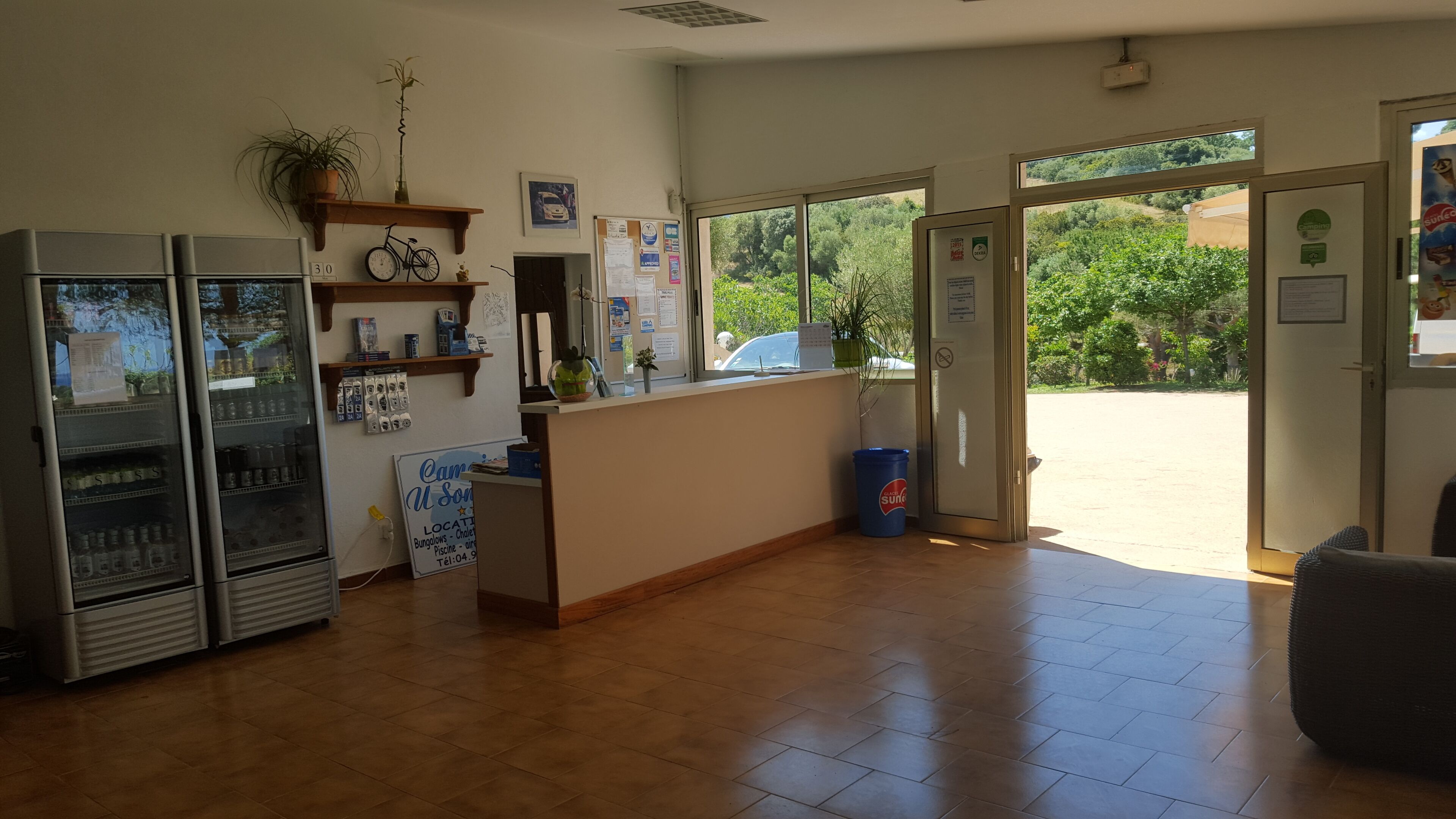 A reception area with a counter, a refrigerator, a potted plant, and a bulletin board with notices.