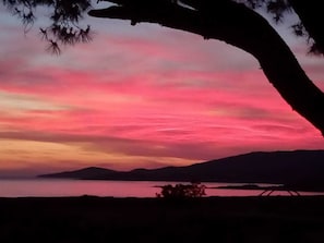 Un coucher de soleil sur une étendue d’eau calme, avec les silhouettes de collines en arrière-plan.