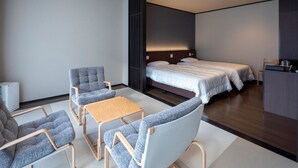 Una habitación de hotel moderna con dos camas, un área de estar con sillas y una mesa, y un escritorio pequeño.