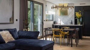Una sala moderna con un sofá azul oscuro, un comedor con sillas amarillas y una cocina con un armario negro.