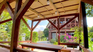 A wooden pavilion with benches, a covered area, and a view of a building with a balcony. - Cottage Muinochichi (Motobu)