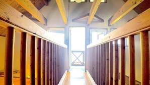 A long, narrow hallway with wooden beams and a wooden floor, leading to a bright, open space. - Cottage Muinochichi (Motobu)