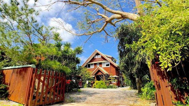 A house with a red roof, surrounded by lush greenery and a clear blue sky. - Cottage Muinochichi (Motobu)