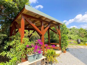 A wooden gazebo with a green roof, surrounded by various plants and flowers.