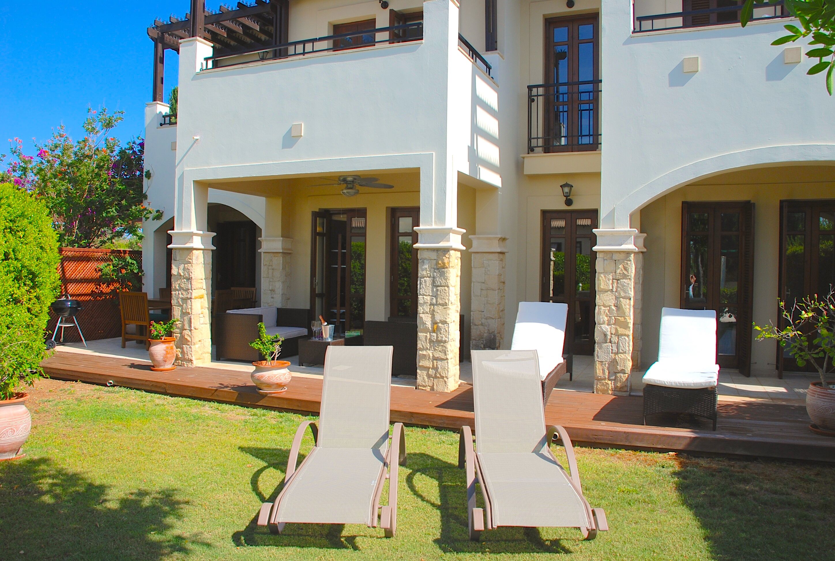 A two-story house with a patio area featuring lounge chairs and potted plants.