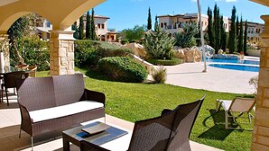 Eine Terrasse mit Korbmöbeln, einer Steinpfeiler und Blick auf einen Swimmingpool und Gebäude im Hintergrund.