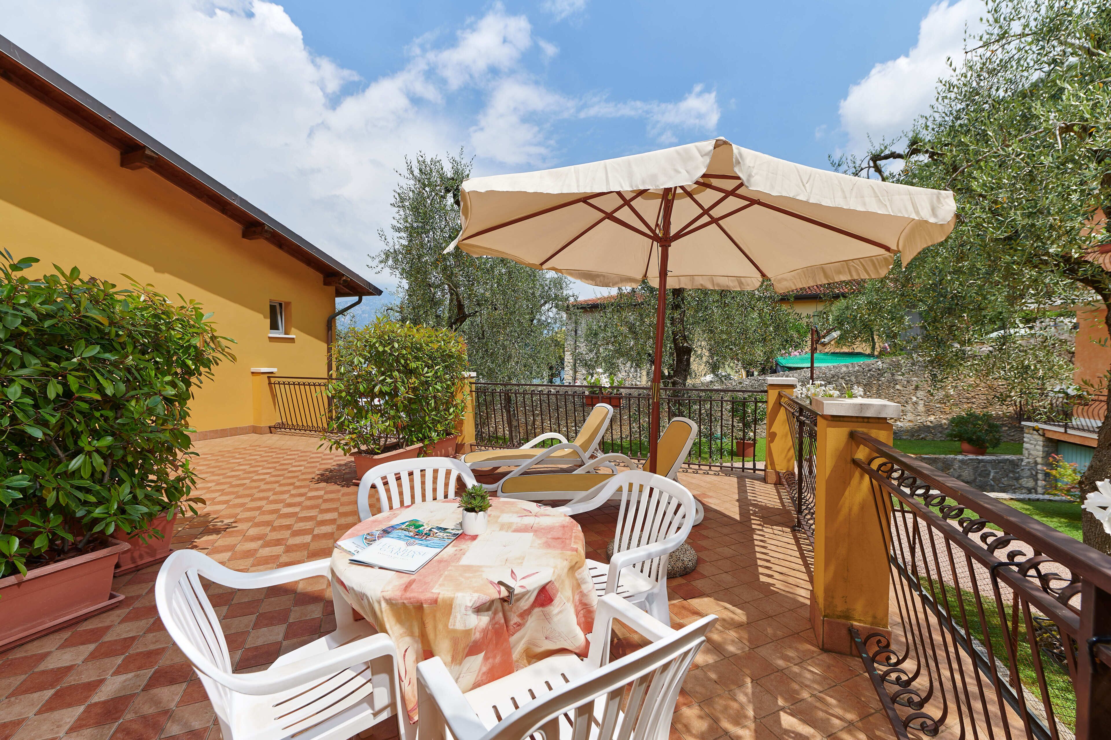 Un patio al aire libre con una mesa y sillas, un paraguas grande y un edificio amarillo al fondo.