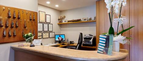 A reception desk with a curved design, a computer monitor, a telephone, and a vase with white flowers.