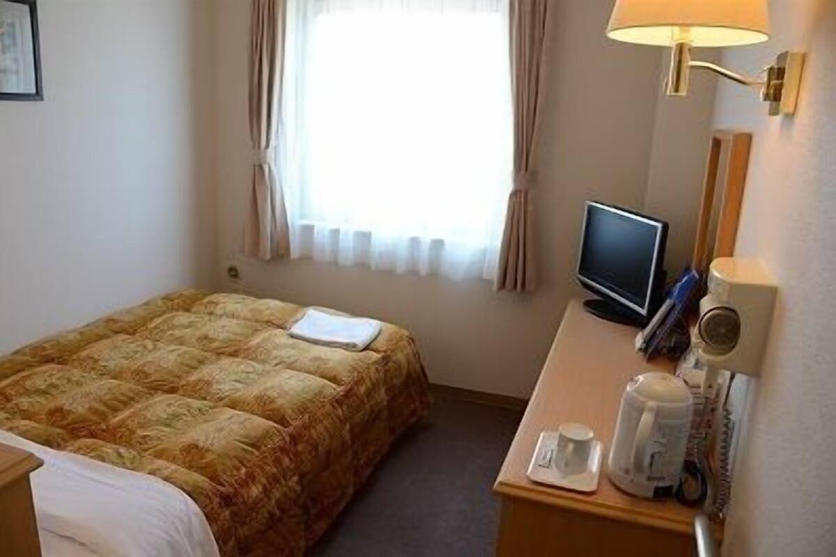 A hotel room with a bed, a desk with a computer, a lamp, and a coffee maker.